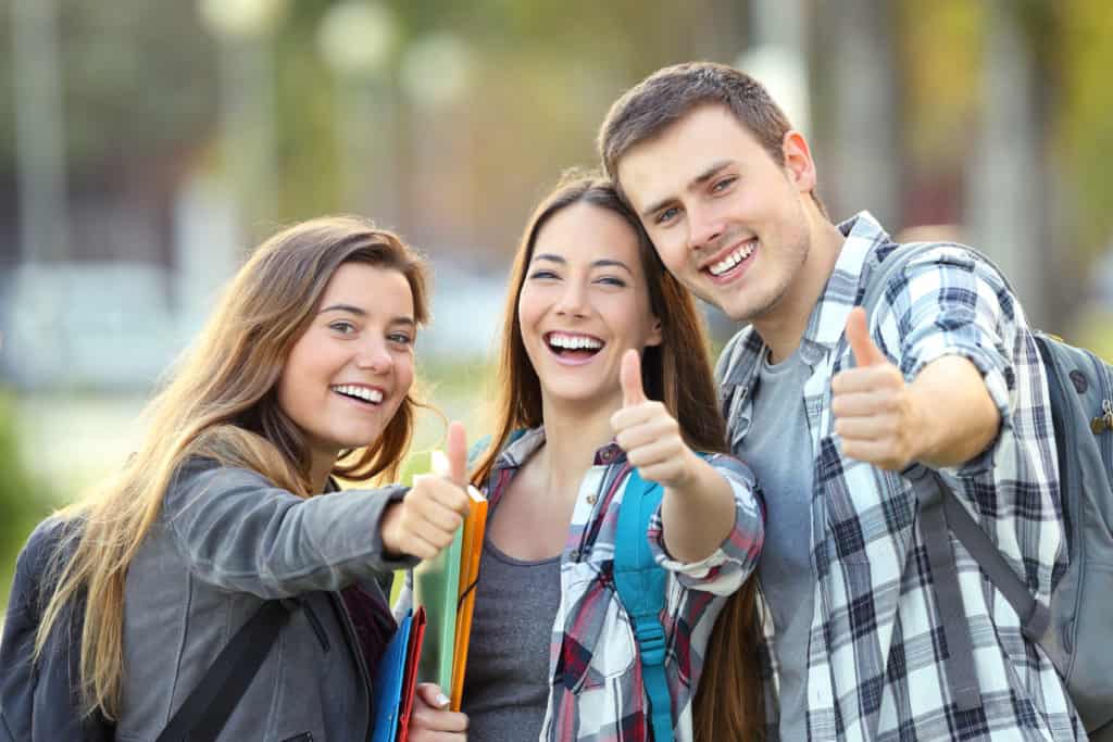 Three happy students with thumbs up Three happy students looking at you with thumbs up in an university campus